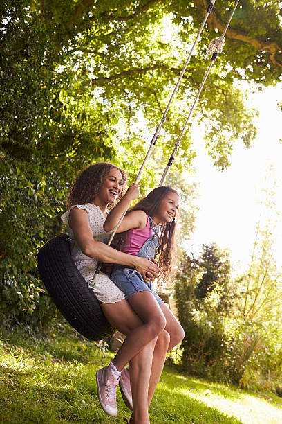 Mother And Daughter Sitting On Tire Swing In Garden Mother And Daughter Sitting On Tire Swing In Garden tire swing stock pictures, royalty-free photos & images