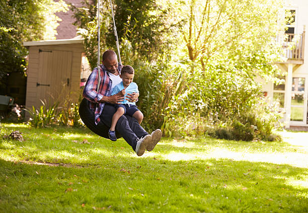 отец и сын весело провести время на шины качели в саду - tire swing стоковые фото и изображения