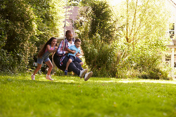 filha empurrando pai e filho em balanço de pneu no jardim - swinging sister family child - fotografias e filmes do acervo