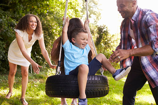родители толкают детей на шины качели в саду - tire swing стоковые фото и изображения