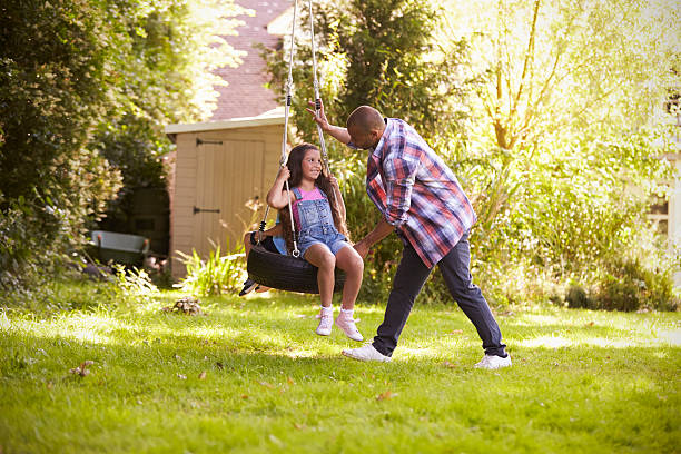 father pushing daughter on tire swing in garden - tire swing imagens e fotografias de stock