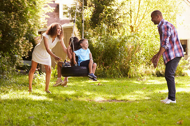parents pushing children on tire swing in garden - tire swing imagens e fotografias de stock