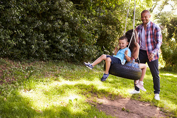 father pushing children on tire swing in garden - tire swing imagens e fotografias de stock