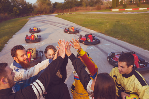 Friends at go karts at amusement park, ready for race doing high five