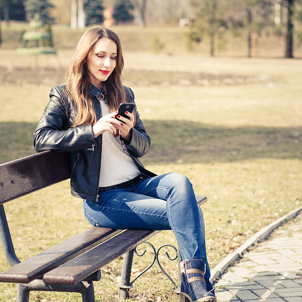 istock Young smiling woman using smartphone in park 613771084