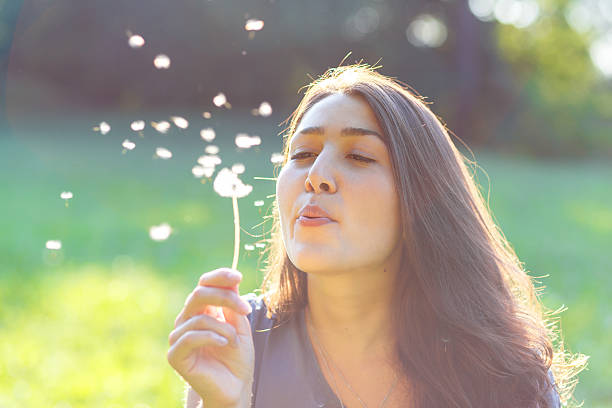 istock Beautiful young woman blowing a dandelion 613772852