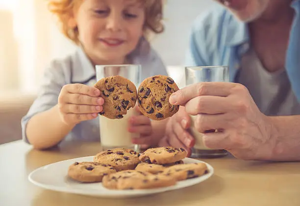 Cropped image of handsome grandpa and grandson drinking milk and eating cookies together at home