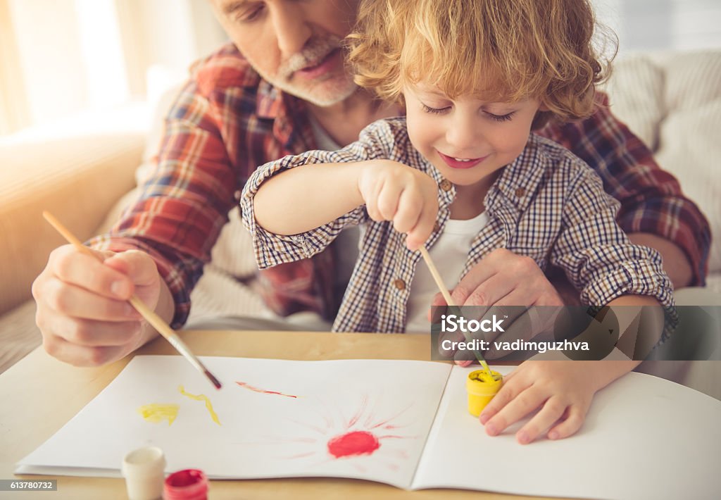 Grandpa and grandson Handsome grandpa and grandson are painting using gouache and smiling while spending time together at home Child Stock Photo