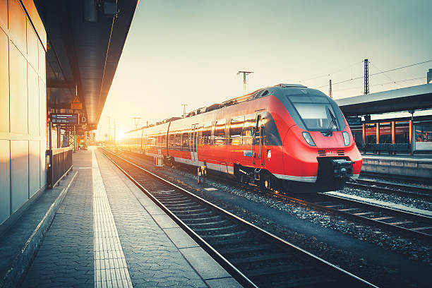 Railway station with beautiful modern red commuter train at suns Beautiful railway station with modern high speed red commuter train at colorful sunset. Railroad with vintage toning. Train at railway platform. Industrial concept. Railway tourism passenger train stock pictures, royalty-free photos & images