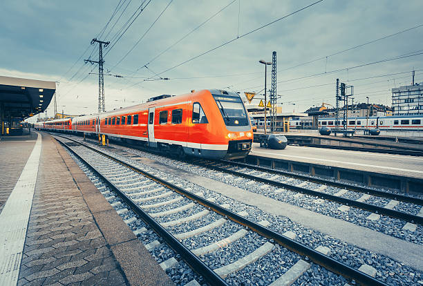 Beautiful railway station with modern high speed red commuter train at colorful sunset. Railroad with vintage toning. Train at railway platform. Industrial concept. Instagram style. Railway tourism