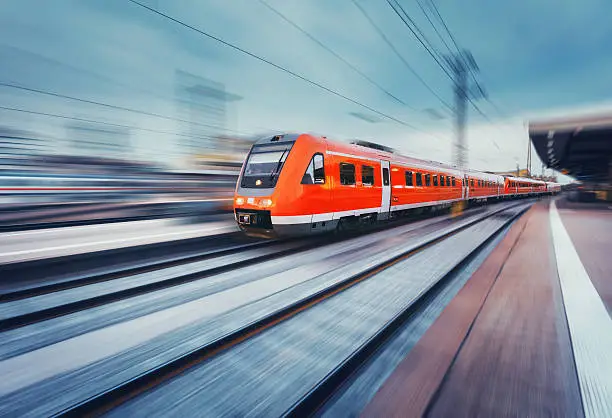 Modern high speed red passenger commuter train in motion at the railway platform. Railway station. Railroad with motion blur effect. Industrial concept landscape with instagram toning. Transportation