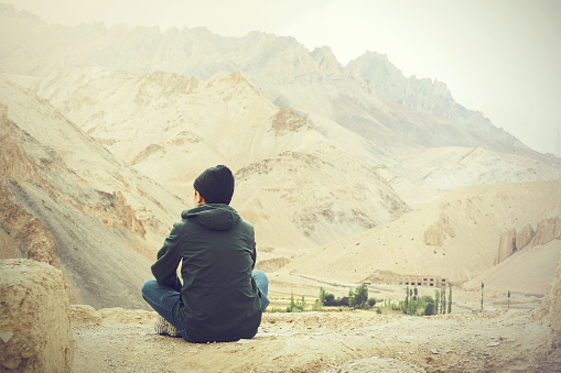 Young male traveler sitting on the sand cliff, thinking about something in Leh, Ladakh, India.