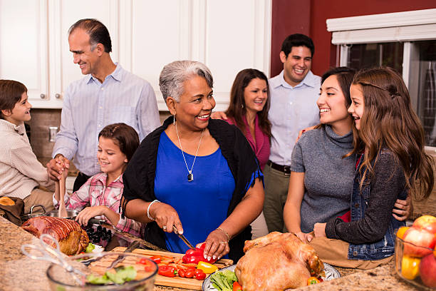 Multi-ethnic family cooks Thanksgiving, Christmas dinner in grandmother's home kitchen. Multi-ethnic, multi-generation family members prepare dinner together in grandmother's home kitchen. Children, mid-adults and senior woman of Latin, African descent, mixed races and Caucasian. Turkey, ham and salad items on kitchen counter. family dinners and cooking stock pictures, royalty-free photos & images