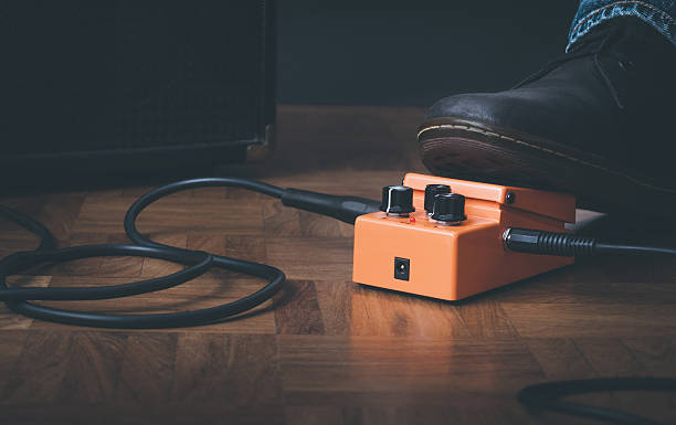 Foot of a rocker young man pushes effect pedal of guitar. Amplifier on the background.