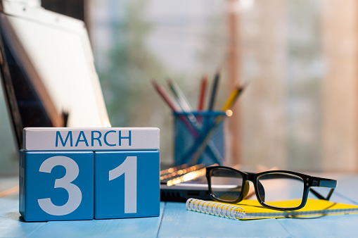 March 31st. Day 31 of month, calendar on business office background, workplace with laptop and glasses. Spring time, empty space for text.