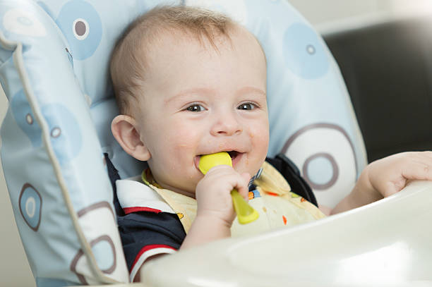 istock Beautiful 9 month baby boy playing with spoon while eating 613875318