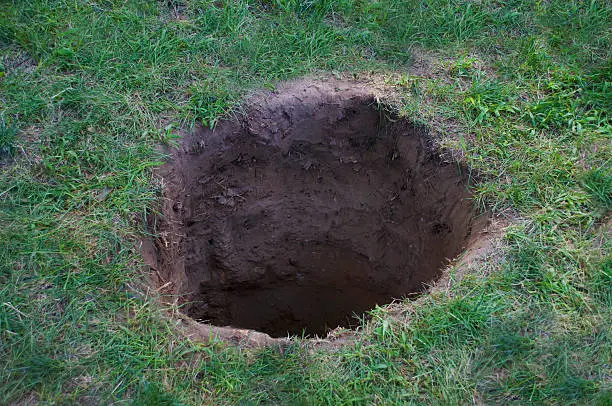Deep dirt hole in ground or lawn