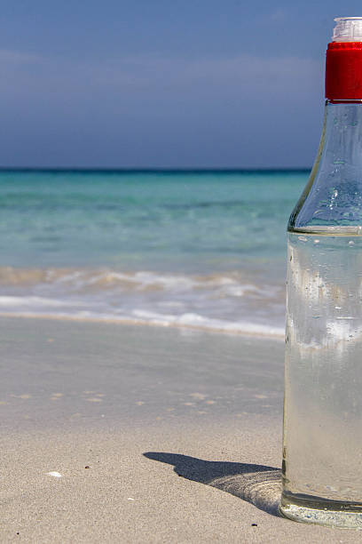 Playas del Este, Cuba - March 28, 2016: A translucid bottle made of glass, full with water, on a sandy beach of the Caribbean sea. In the bottom, the blue navy and turquoise waters of the sea.