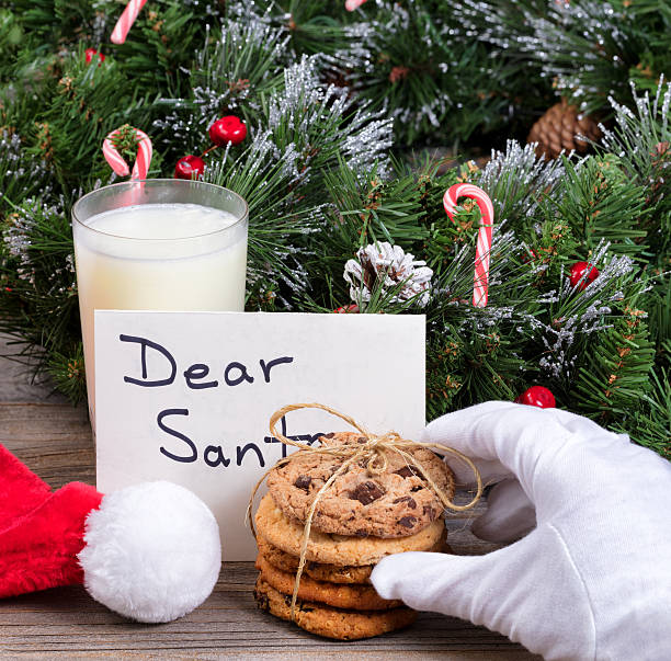 istock Santa Claus hand reaching for a cookie with holiday decorations 613882208