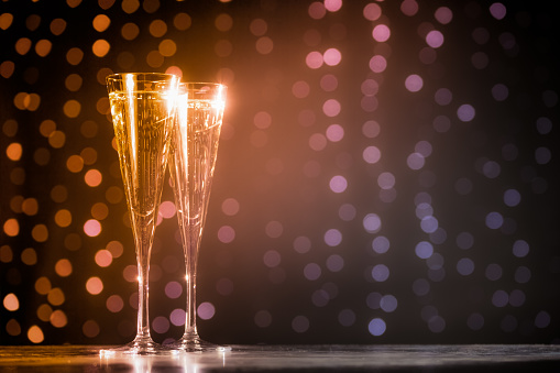 Two glasses of champagne on dark bokeh background. Holiday concept. Festive bokeh background. Horizontal, toned, warm tone, orange to pink