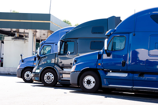Modern popular models of heavy trucks are shades of blue in a row on a truck stop for drivers' rest and refueling of vehicles for the further movement for delivery commercial goods in accordance with the schedule drawn up and route
