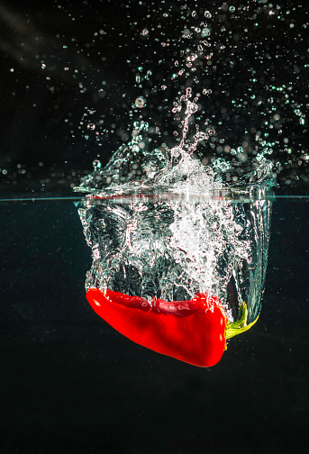 Fresh red chile pepper splashing into water 