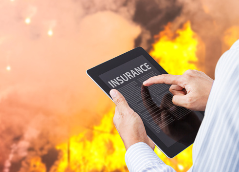 Man pointing at insurance wording on tablet with fire background