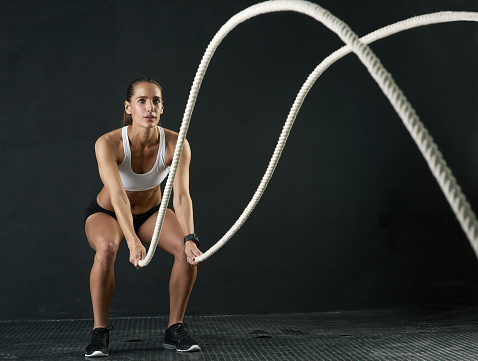 Studio shot of an attractive young woman working out with heavy ropes against a dark background