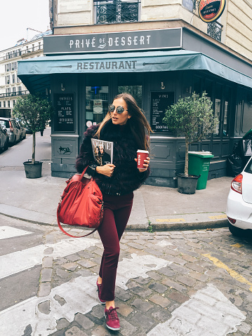Paris, France - April 28, 2016: Fashionable young woman is walking on the zebra crossing with the Vogue magazine underarm and a cup of coffee