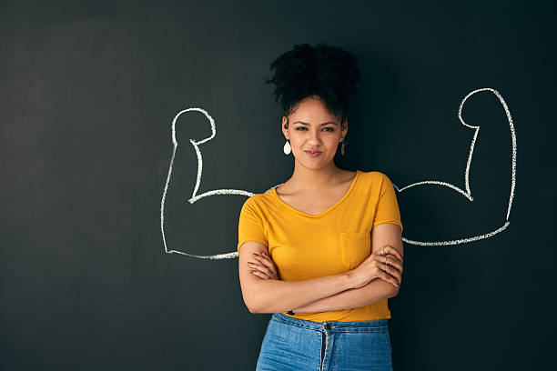 I am a strong woman! Shot of a woman posing with a chalk illustration of flexing muscles against a dark background women empowerment stock pictures, royalty-free photos & images