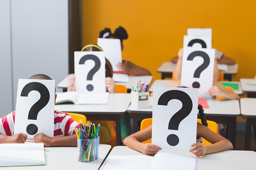 School kids covering their face with question mark sign in classroom at school