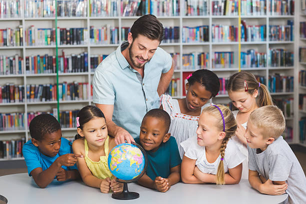 istock Pupils and teacher looking at globe in library 614013726