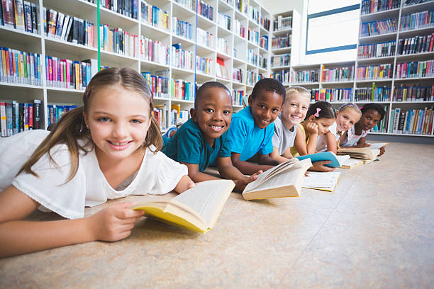 istock Smiling school kids lying on floor reading book in library 614013860