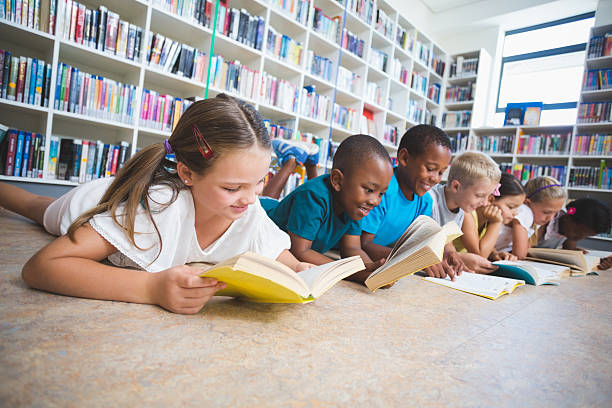 School kids lying on floor reading book in library stock photo