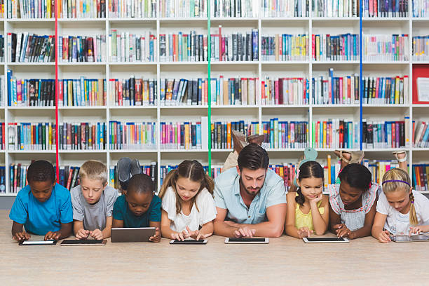 Teacher and kids lying on floor using digital tablet Teacher and kids lying on floor using digital tablet in library at elementary school rows of books stock pictures, royalty-free photos & images