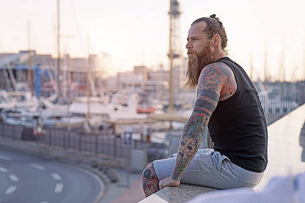 istock Handsome bearded hooded man sitting alone by urban harbour 614013938