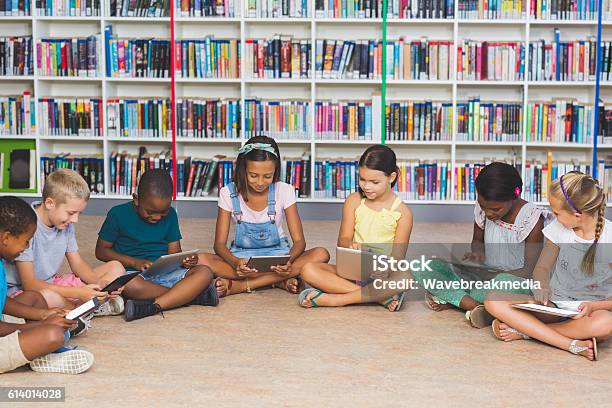 School Kids Sitting On Floor Using Digital Tablet In Library Stock Photo - Download Image Now