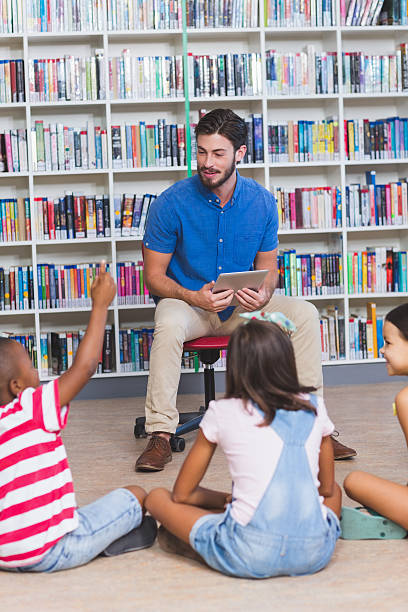 istock Teacher teaching kids on digital tablet in library 614014048