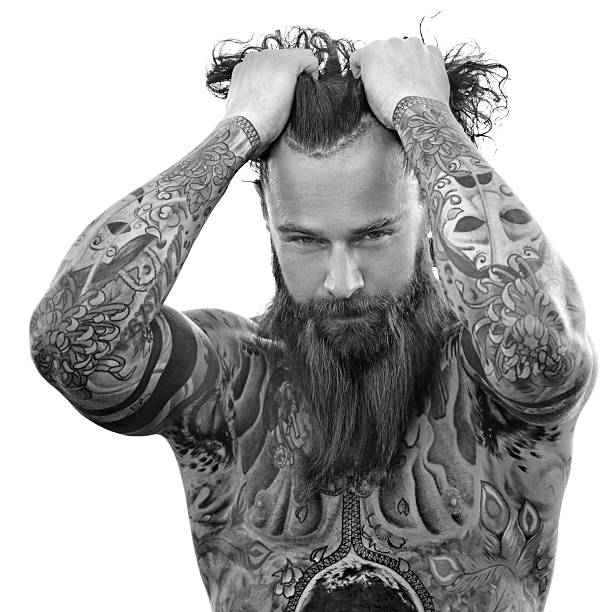 Heavily tattooed bare chested handsome male standing in warrior stance Heavily tattooed bare chested handsome male standing in warrior stance chest tattoo men stock pictures, royalty-free photos & images