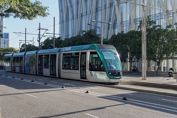 Seville, Spain - March 10, 2025: A modern tram stands on tracks in a historic street while pedestrians walk by. The Giralda Tower can be seen in the background.