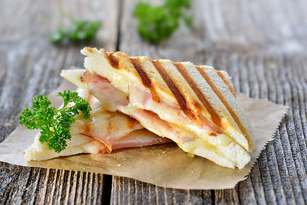 Toasted double panini Pressed and toasted double panini with ham and cheese served on sandwich paper on a wooden table panino stock pictures, royalty-free photos & images