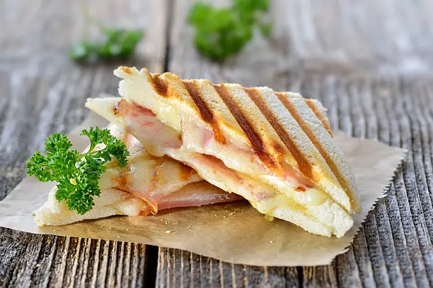 Pressed and toasted double panini with ham and cheese served on sandwich paper on a wooden table