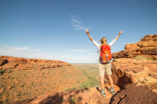 Young woman hiking celebrates achievement on top of the rock, landscape of kings canyon in outback, red centre of Australia.