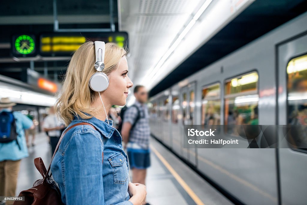 Young woman in denim shirt at the underground platform, waiting Beautiful young blond woman in denim shirt with earphones, standing at the underground platform, waiting to enter a train Commuter Stock Photo