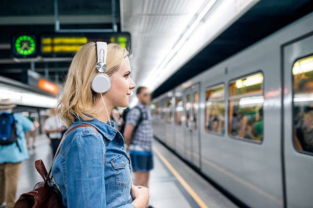 Young woman in denim shirt at the underground platform, waiting Beautiful young blond woman in denim shirt with earphones, standing at the underground platform, waiting to enter a train commuter stock pictures, royalty-free photos & images