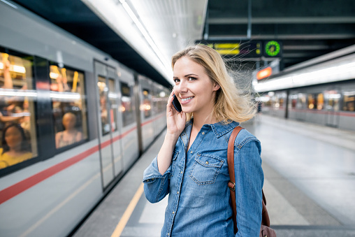 Beautiful young blond woman in denim shirt with smartphone making phone call. Standing at the underground platform, waiting to enter a train.