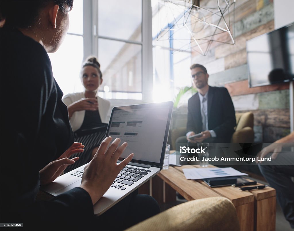 Businesswoman discussing business strategy with colleagues Business woman with laptop discussing business strategy with colleagues. Businesspeople having a meeting. Candid Stock Photo