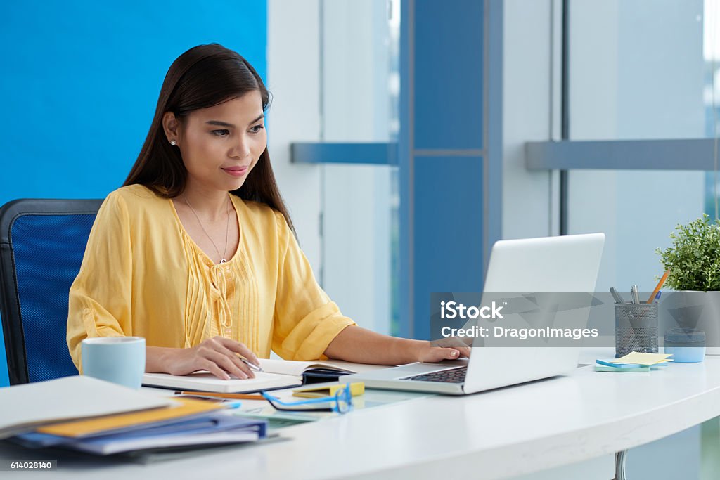 Working on computer Pretty Filipina young woman working on laptop in office Filipino Ethnicity Stock Photo