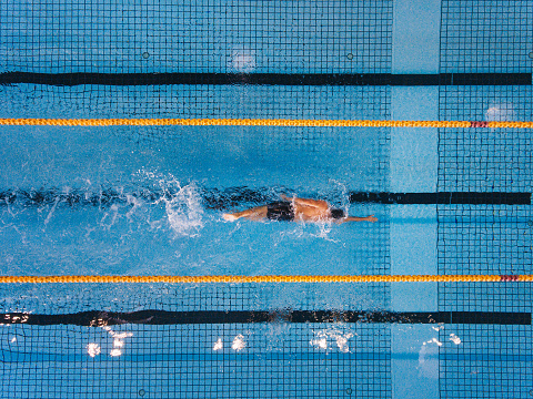 Mid race butterfly stroke swimming race in a olympic size swimingpool. Referee standing by the side.