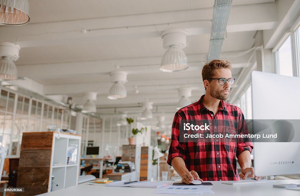 Young man working on computer in modern workplace Shot of young businessman in casual clothes at modern startup business office space, working on  desktop computer. Office Stock Photo